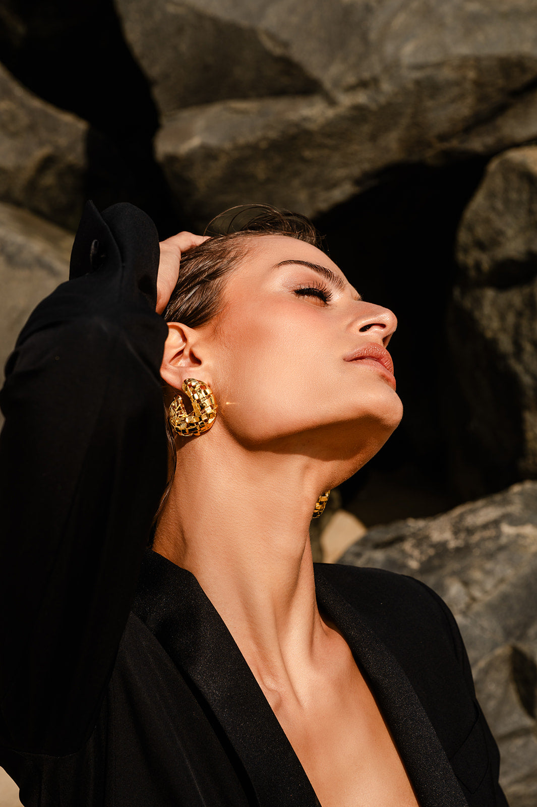 Model in black wearing Woven C Earring with rocks in the background