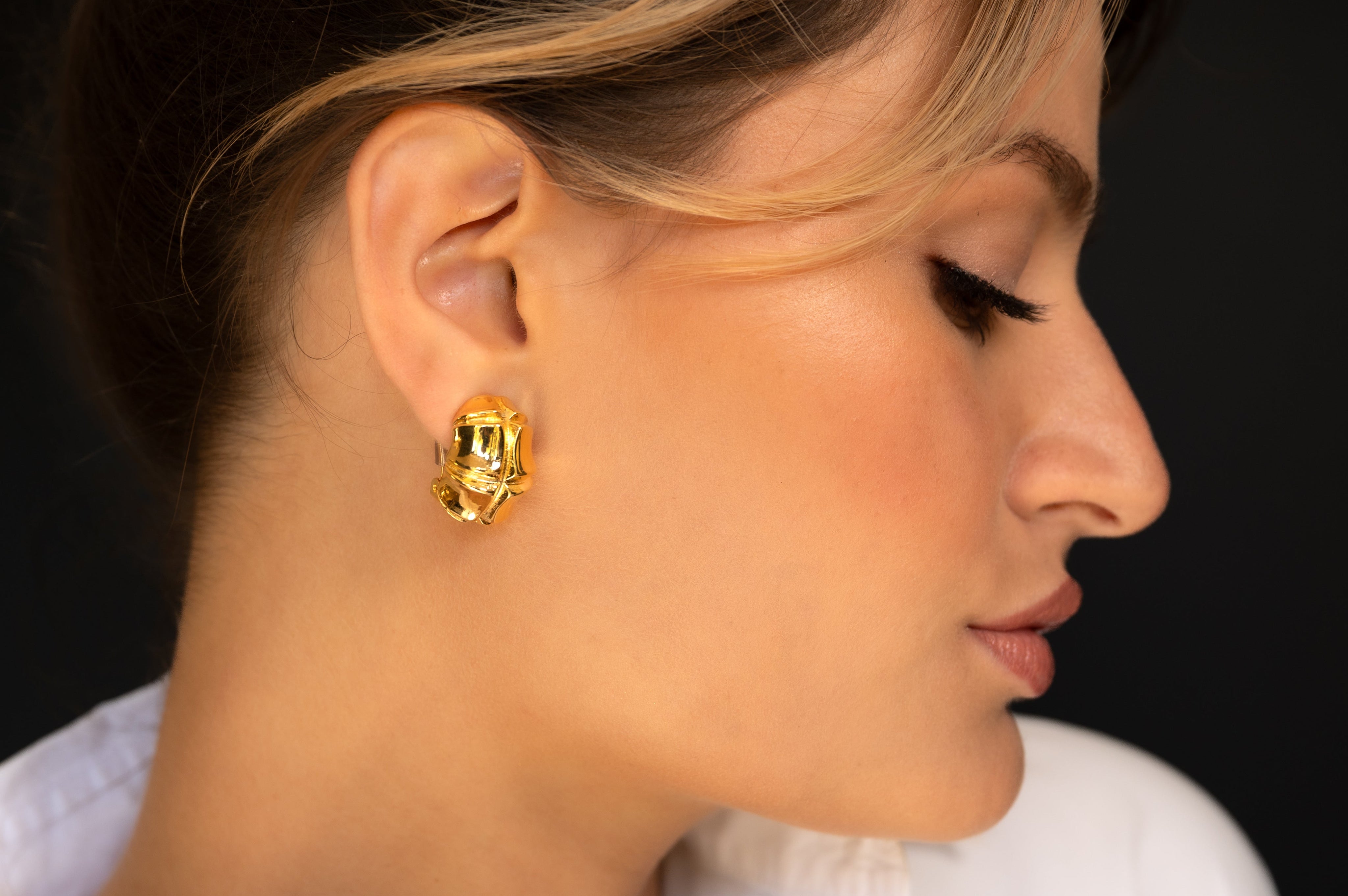 Woman wearing gold hoop earrings with a black background