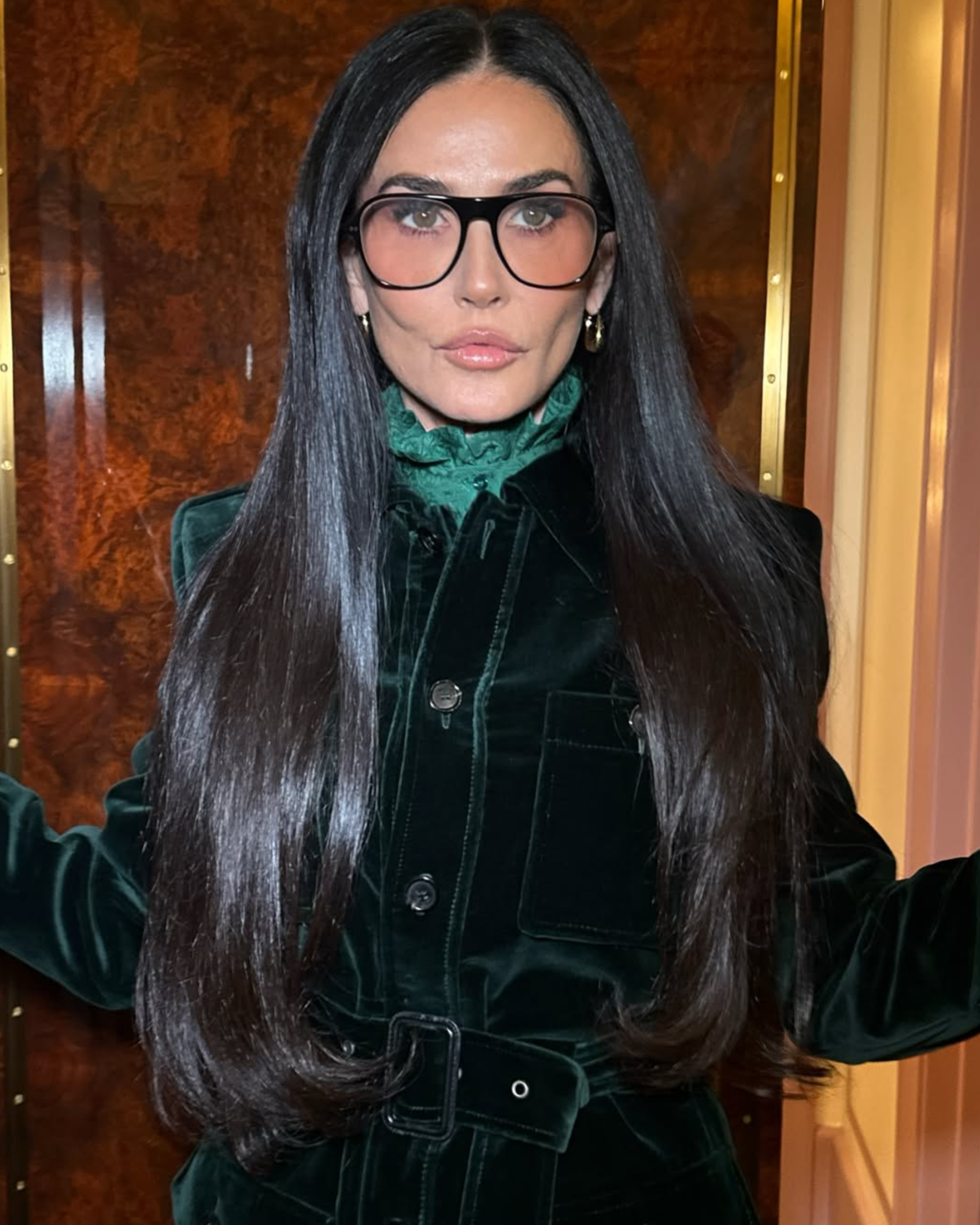 wearing a dark green coat and glasses indoors.