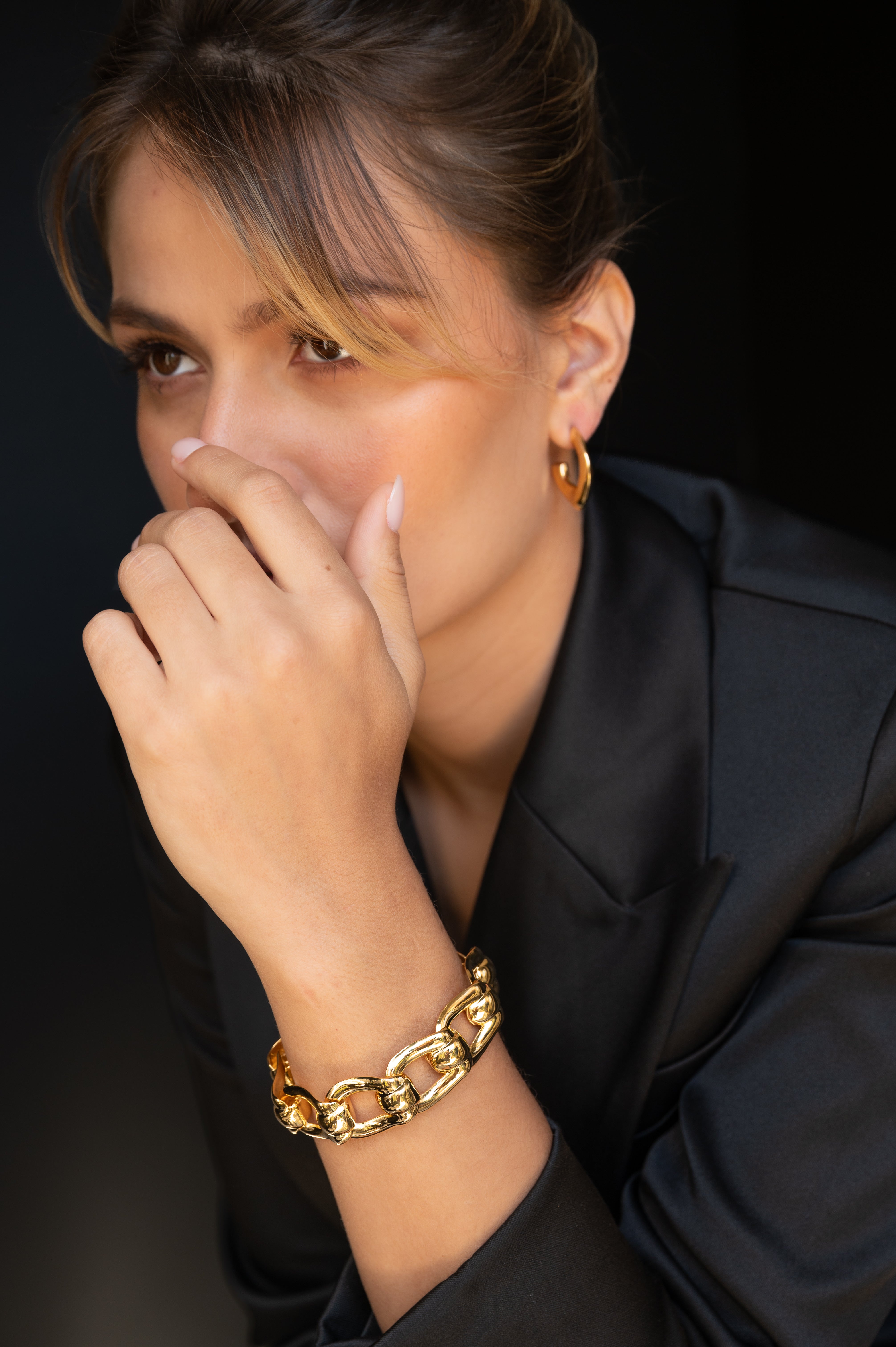 Woman wearing a gold bracelet and earring against a black background